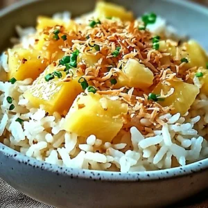 Bowl of creamy coconut pineapple rice garnished with fresh pineapple and coconut shavings.